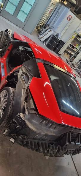 Red Corvette seen from above at the rear corner, bumper cover off, mid-repair in the shop